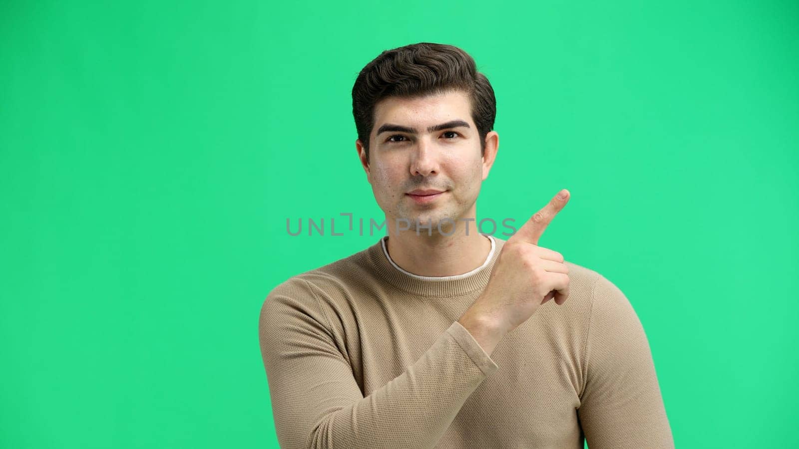 A man, close-up, on a green background, points to the side.