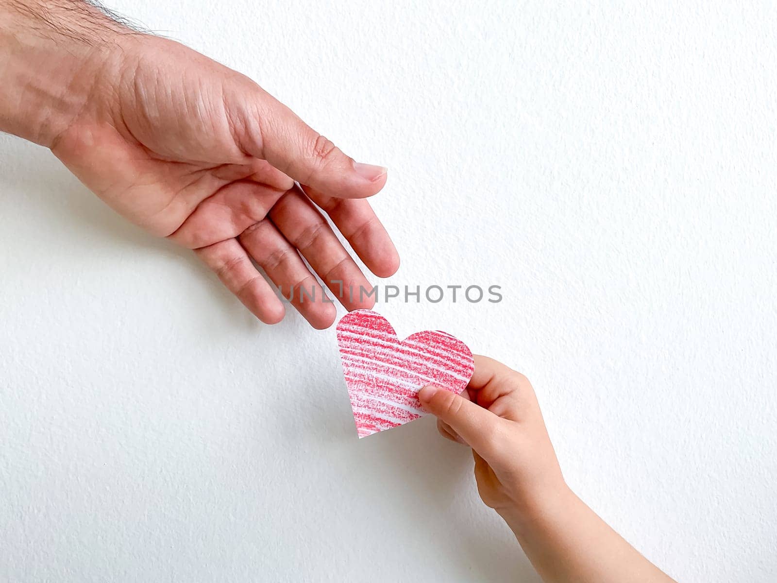 Adult hand giving striped pink paper heart to childs hand, concept of love, care, and family bonding with copy space. Can be utilized for materials about parenting, child development, and family relationships. It is ideal for use in educational contexts, social services, and psychology resources. High quality photo
