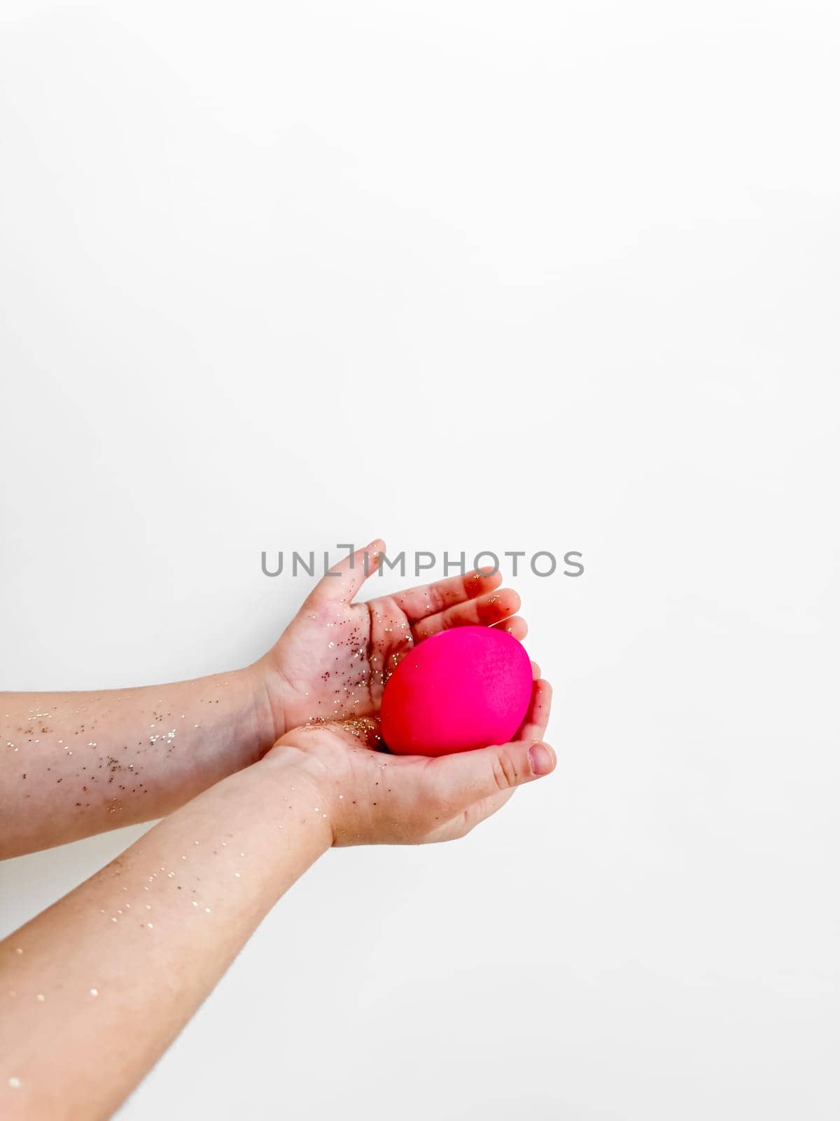 Hands holding a pink egg with glitter, Easter preparation and festive activity concept on a white background with copy space. For Easter themed creative content, and family activity ideas. High quality photo