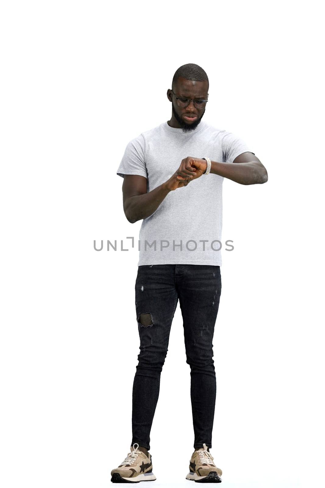 A man, full-length, on a white background, looks at his watch.