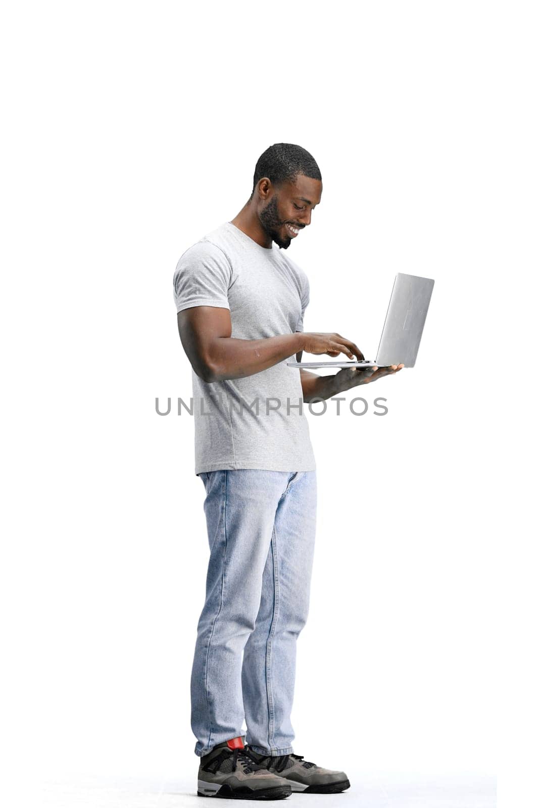 A man, full-length, on a white background, uses a laptop.