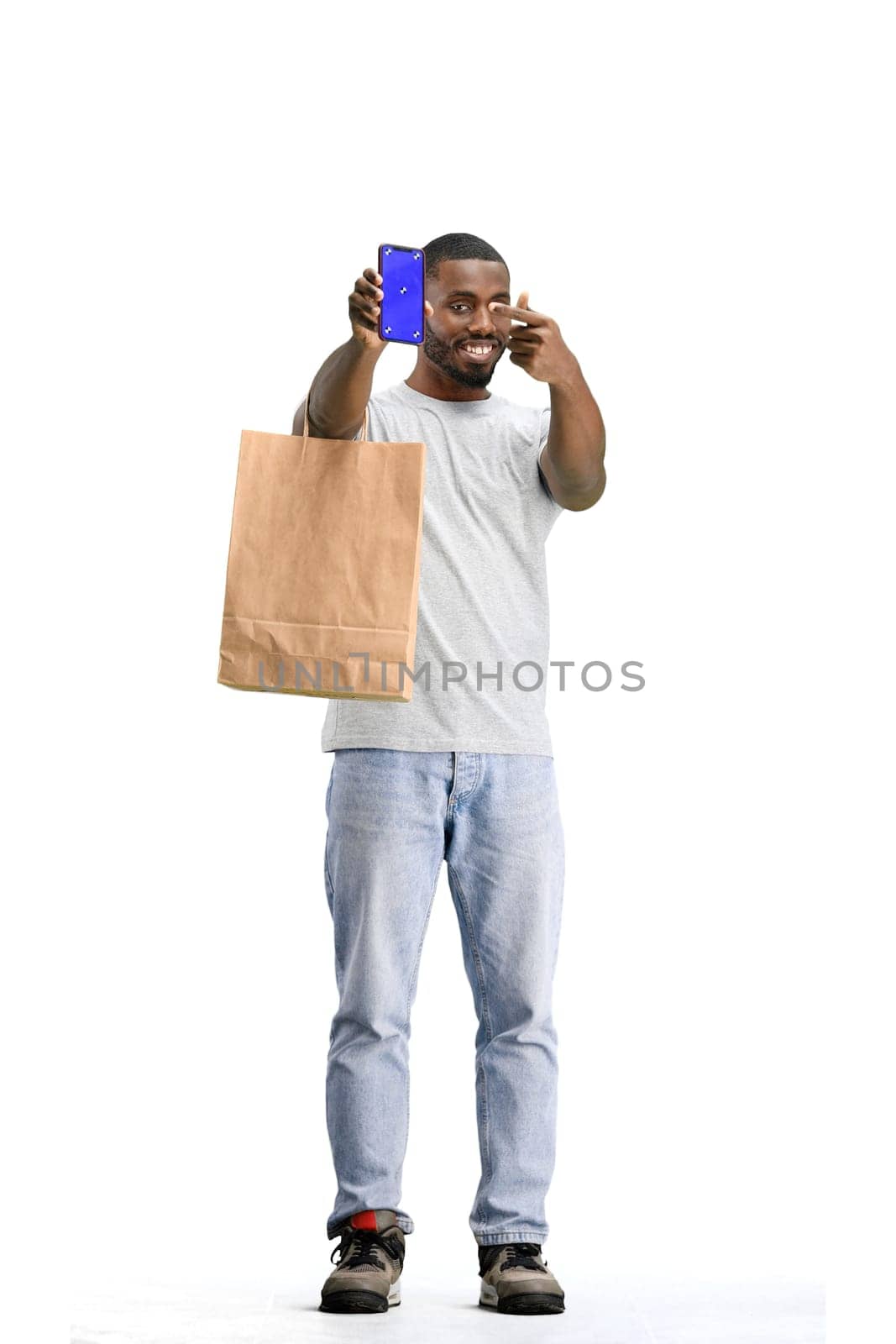 A man, full-length, on a white background, with bags, shows a phone by Prosto