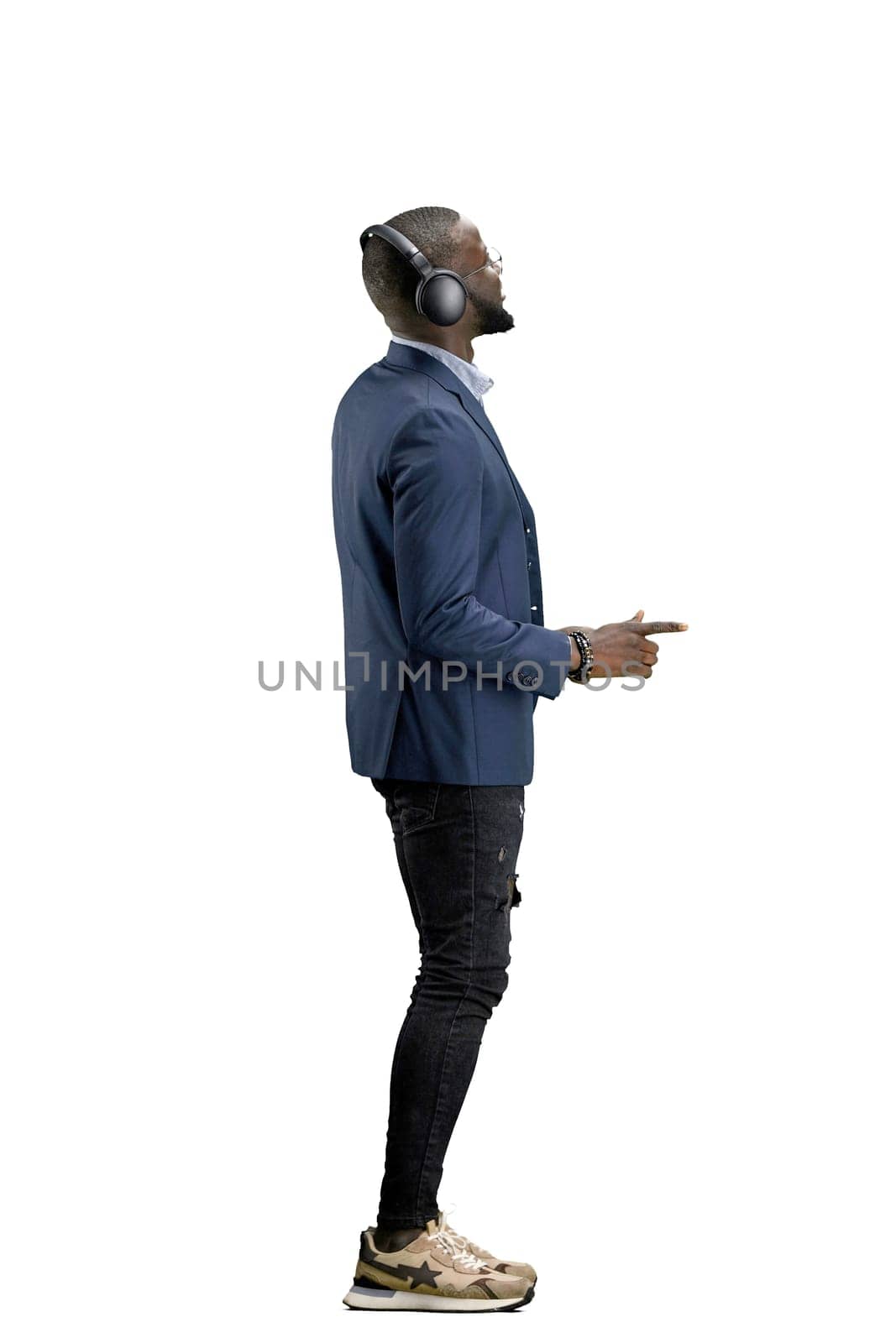 A man, full-length, on a white background, listening to music with headphones.