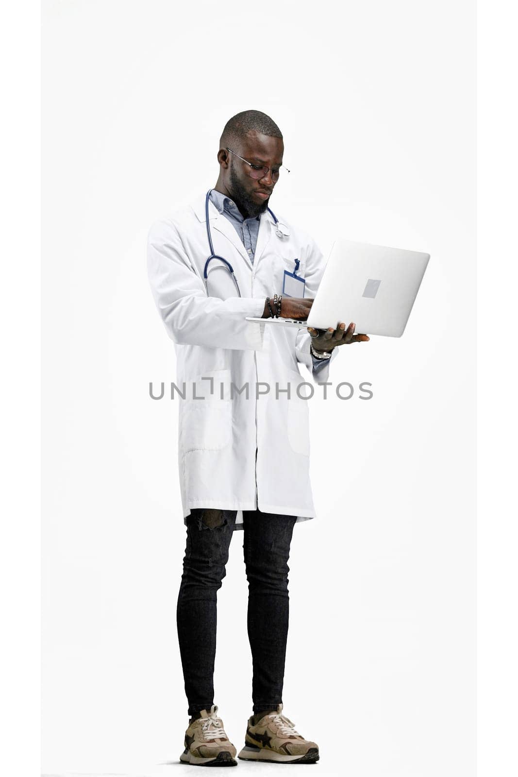 The doctor, in full height, on a white background, uses a laptop.