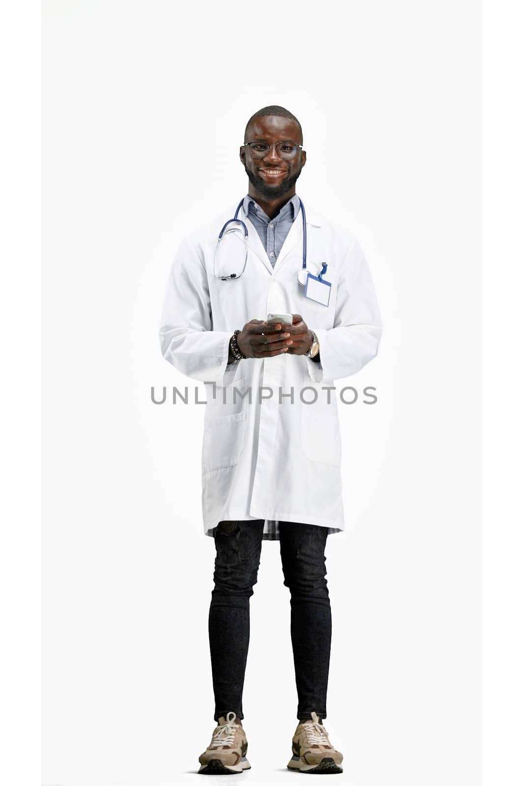 The doctor, in full height, on a white background, uses a phone.