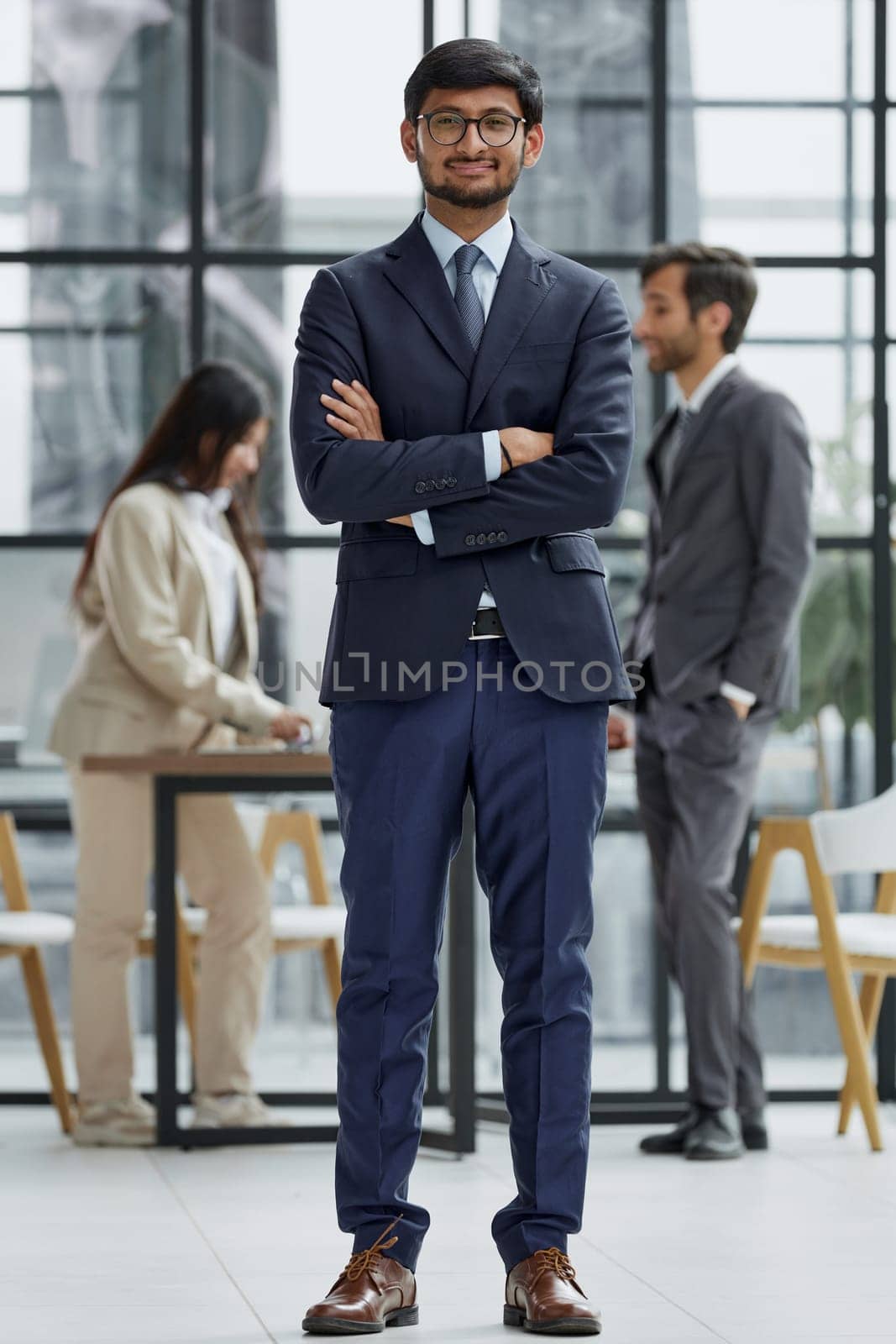 Handsome young business man in glasses standing confidently in the office by Prosto
