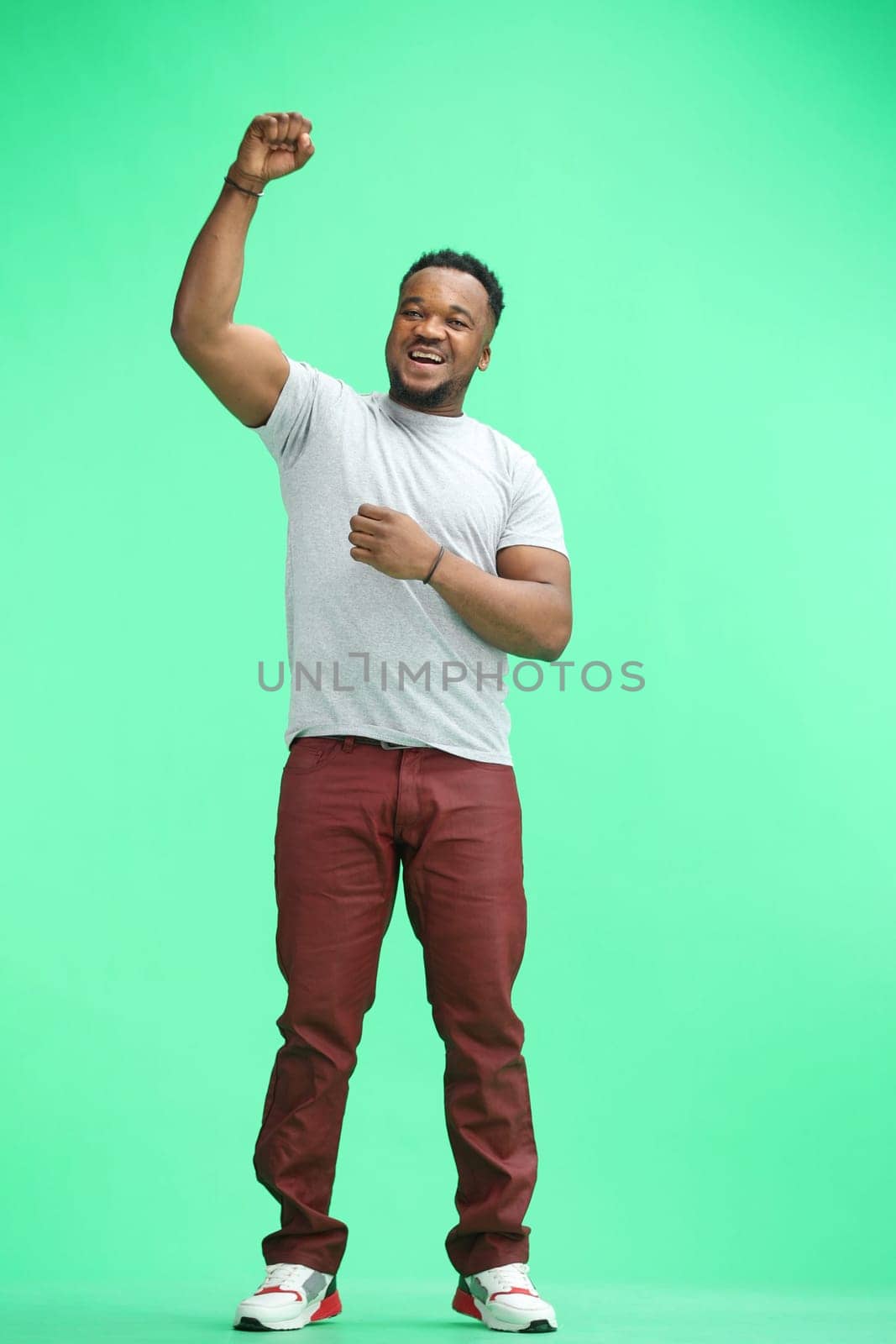 A man, full-length, on a green background, rejoicing.