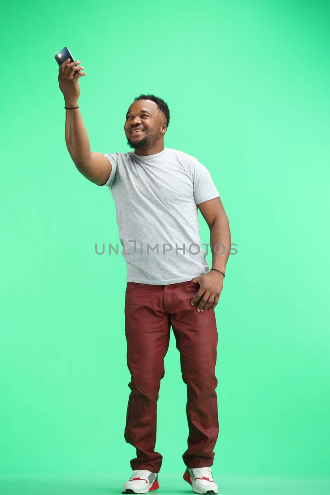 Man, full-length, on a green background, waving a phone.