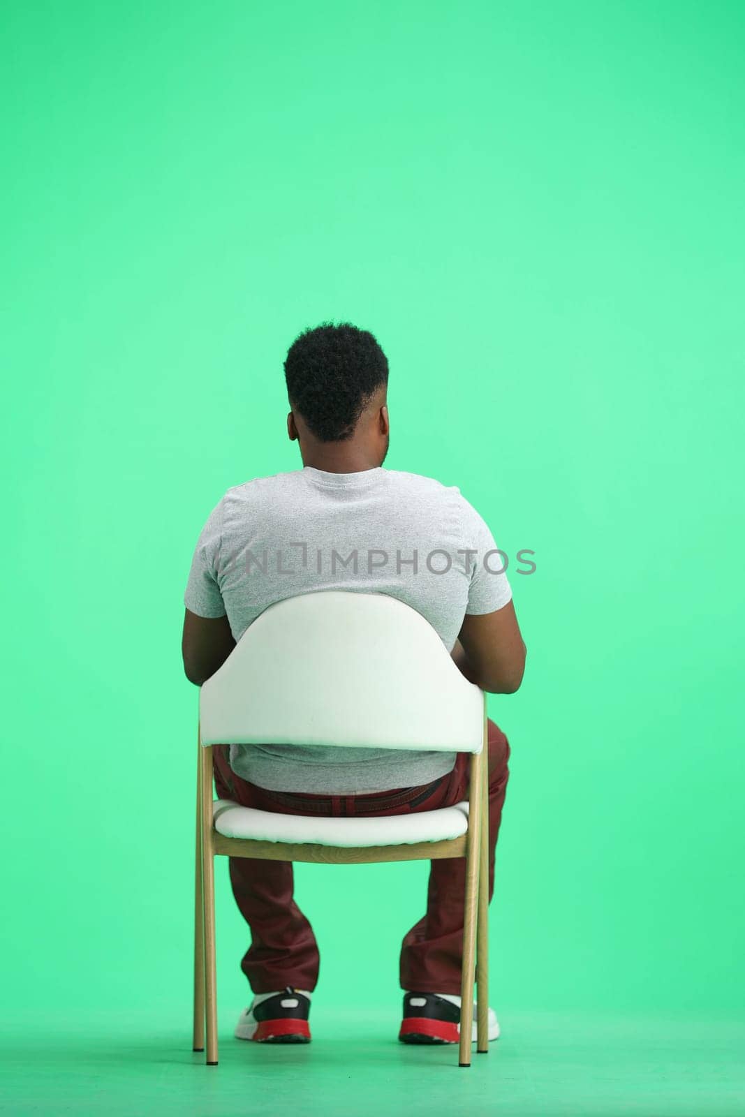 Man, on a green background, sitting on a chair.