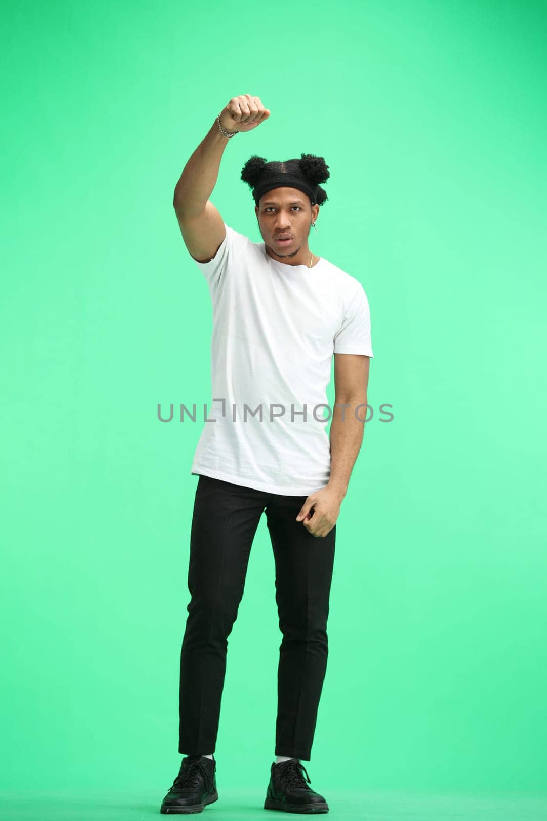 A man, full-length, on a green background, raised his hand up.