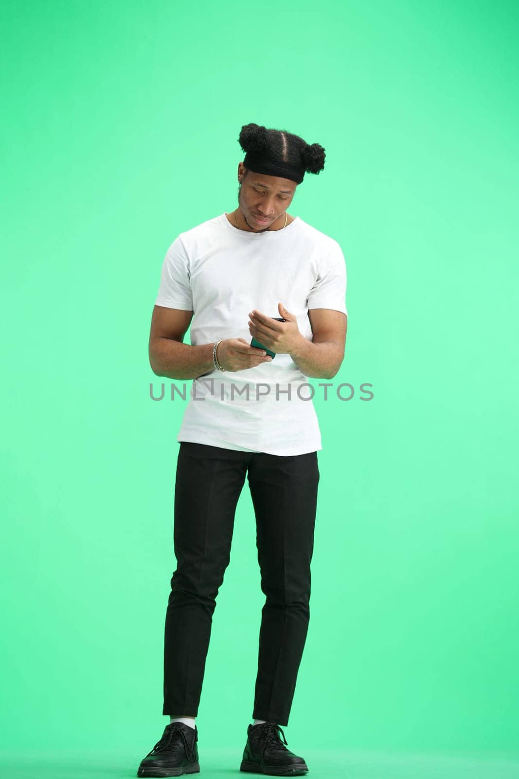 A man, full-length, on a green background, uses a phone by Prosto