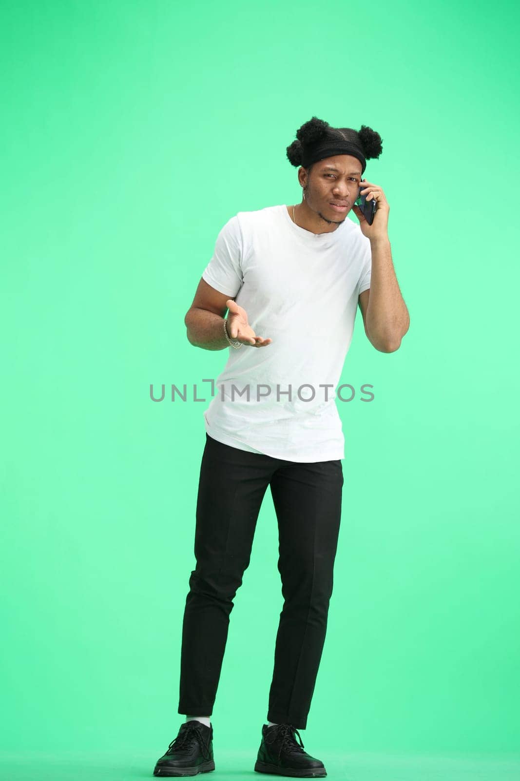 A man, full-length, on a green background, talking on the phone.