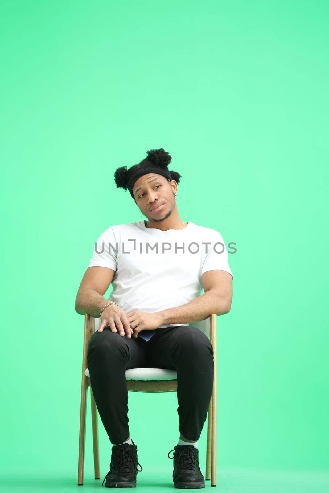 A man, on a green background, sitting on a chair by Prosto