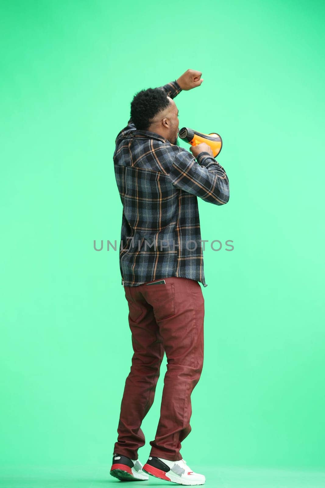 A man, full-length, on a green background, with a megaphone.