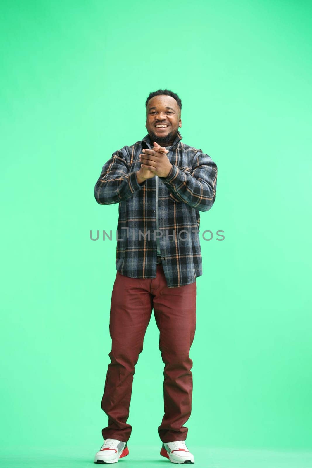 A man, full-length, on a green background, claps.