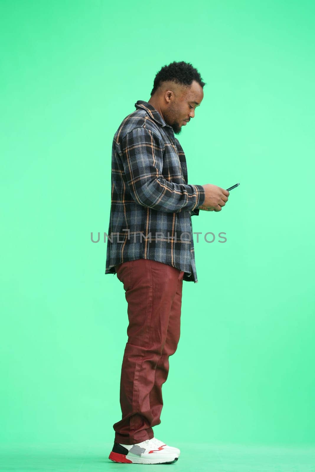 A man, full-length, on a green background, uses a phone by Prosto