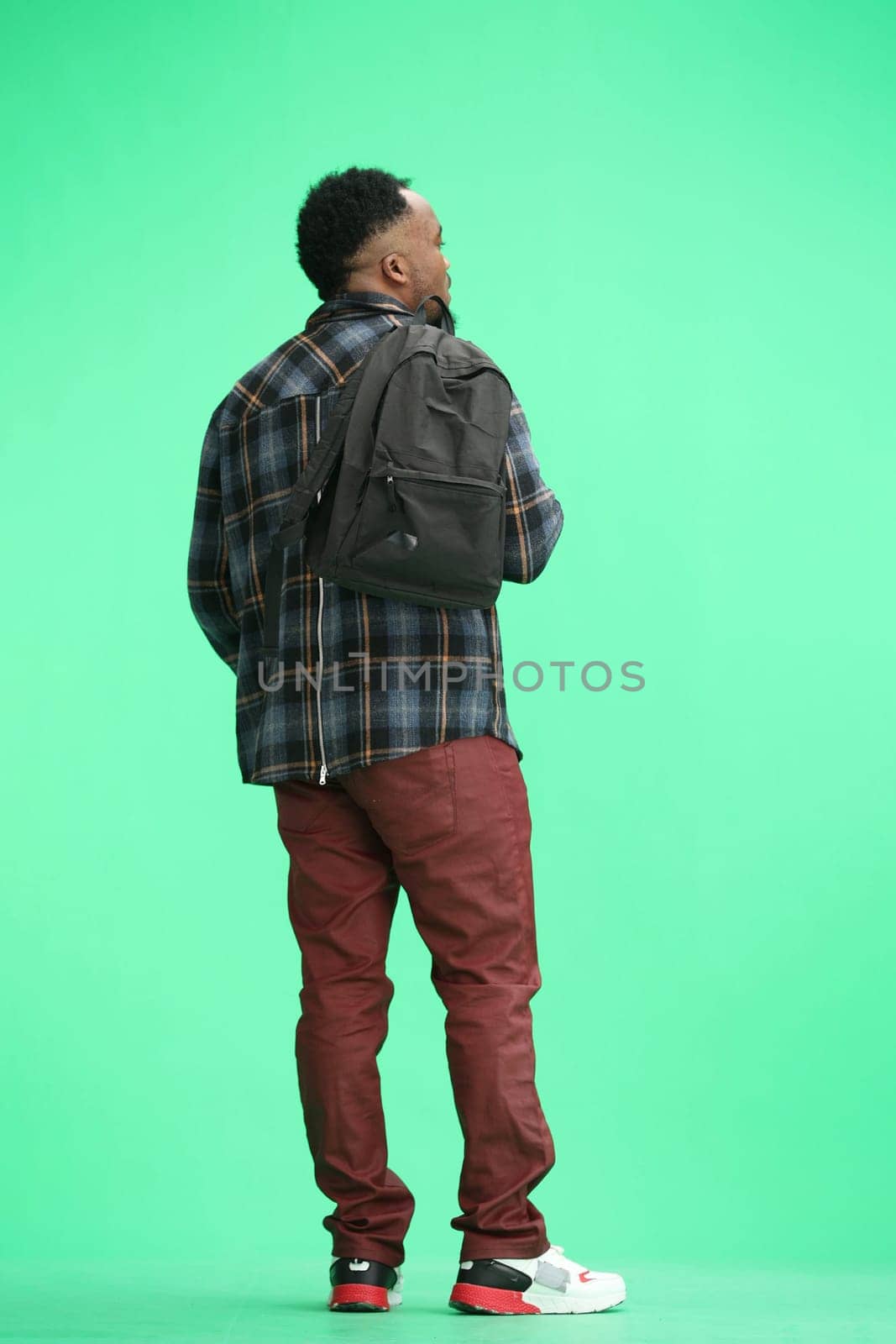 A man, full-length, on a green background, with a backpack.
