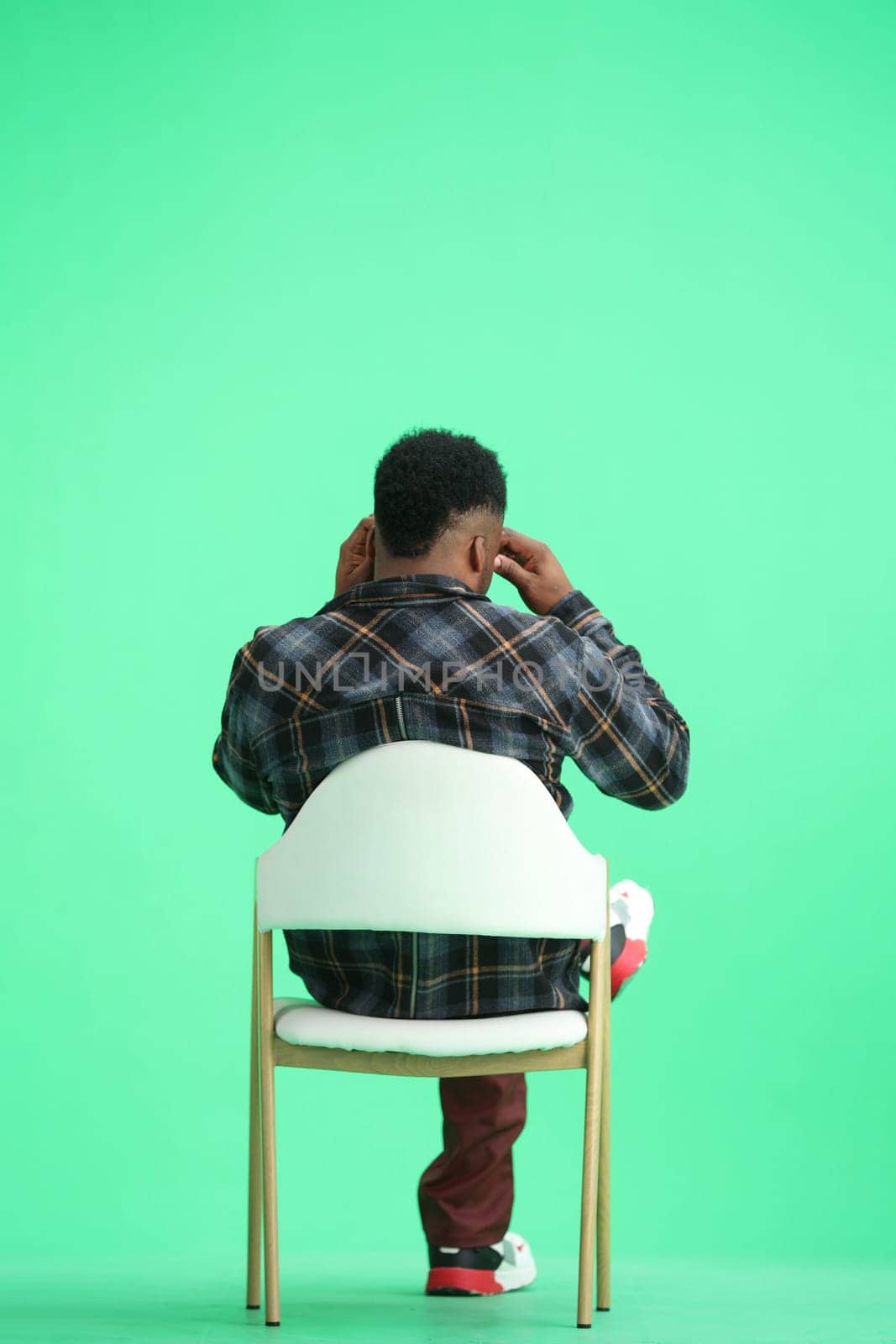 A man, on a green background, sitting on a chair.