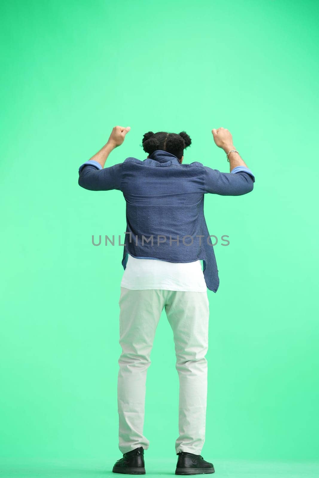 A man, full-length, on a green background, raised his hands up.