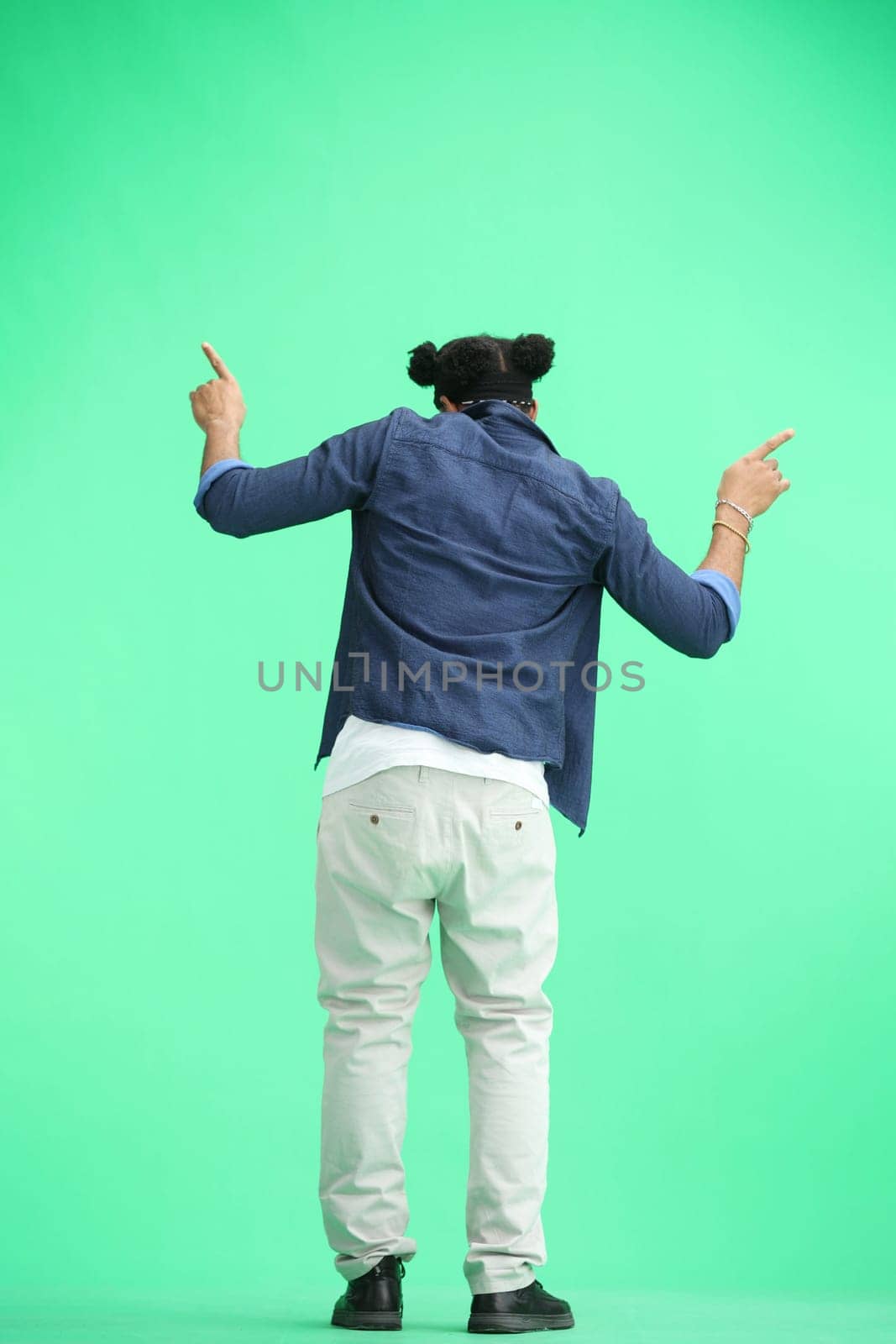 A man, full-length, on a green background, dancing.