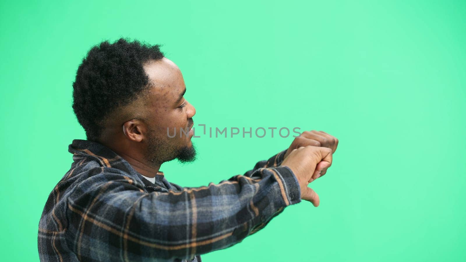 A man, close-up, on a green background, shows his thumbs down.