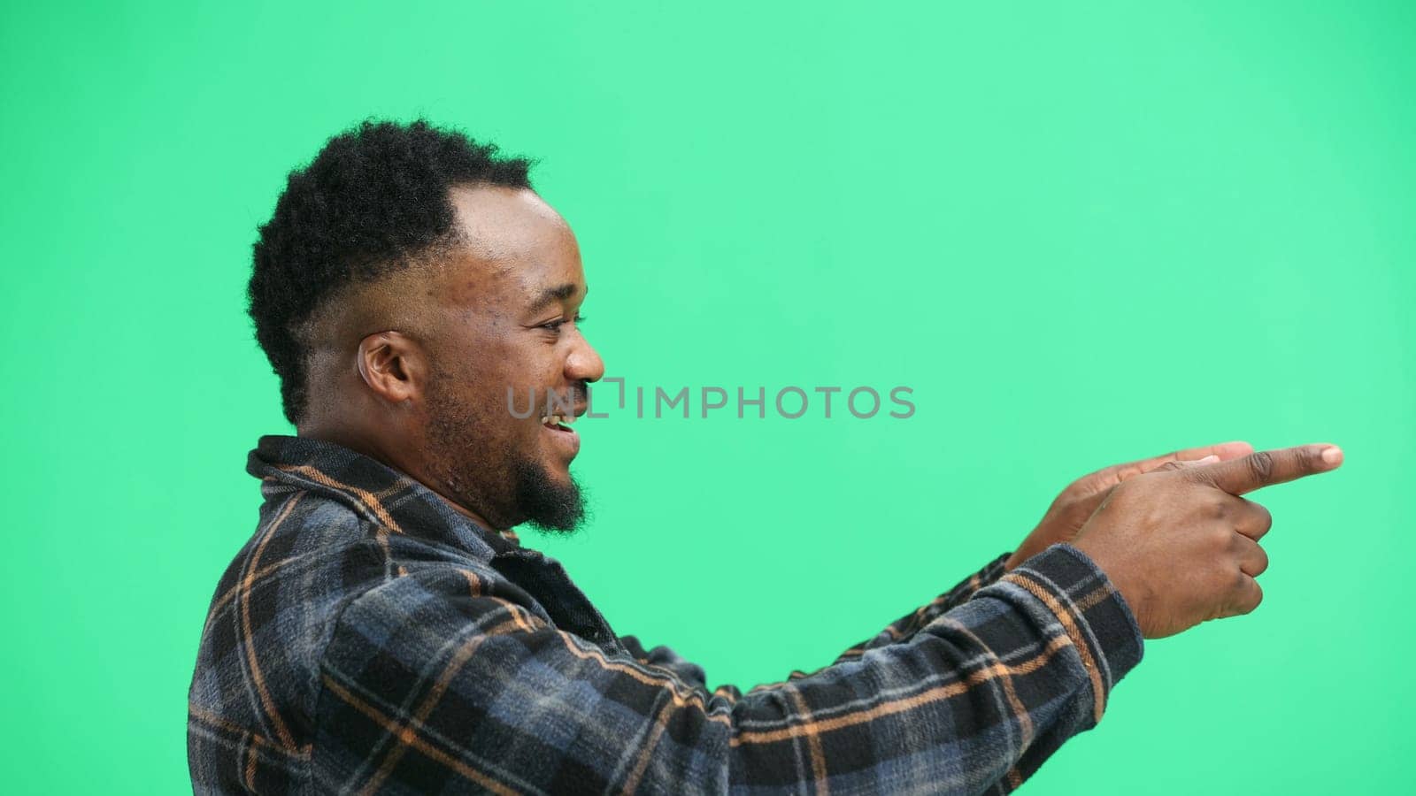 A man, close-up, on a green background, points to the side.