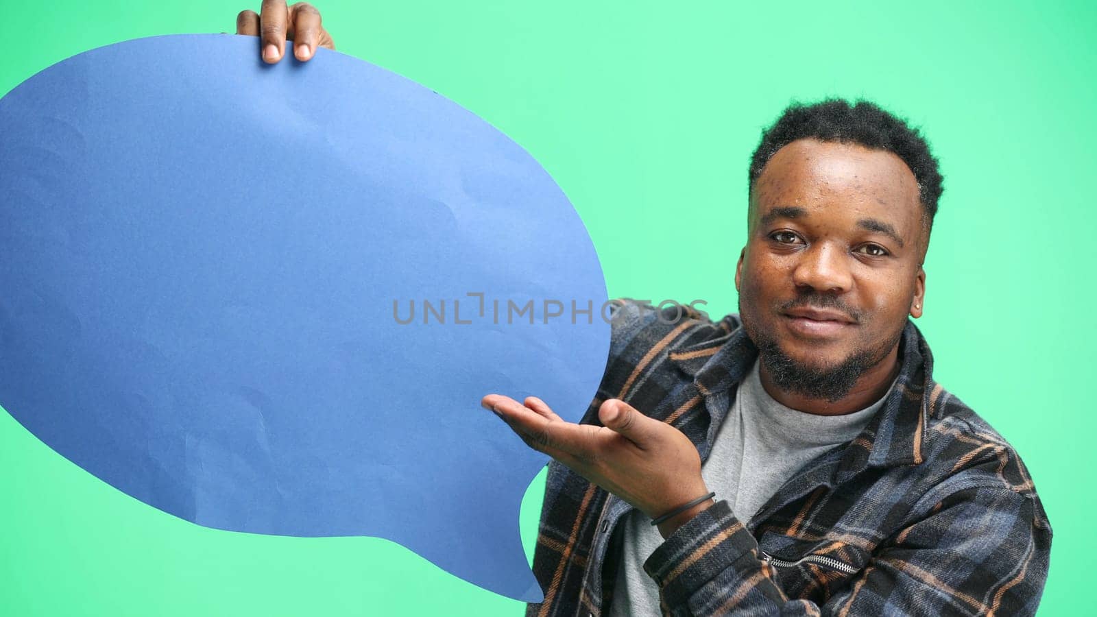 A man, close-up, on a green background, shows a blue comment sign.