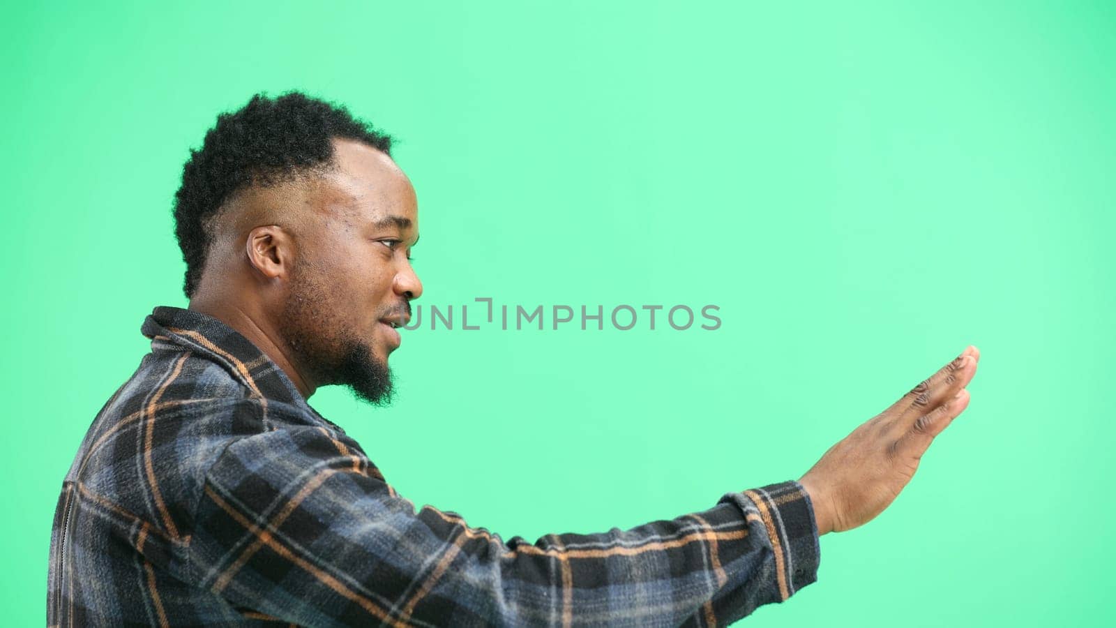 A man, close-up, on a green background, shows a stop sign.