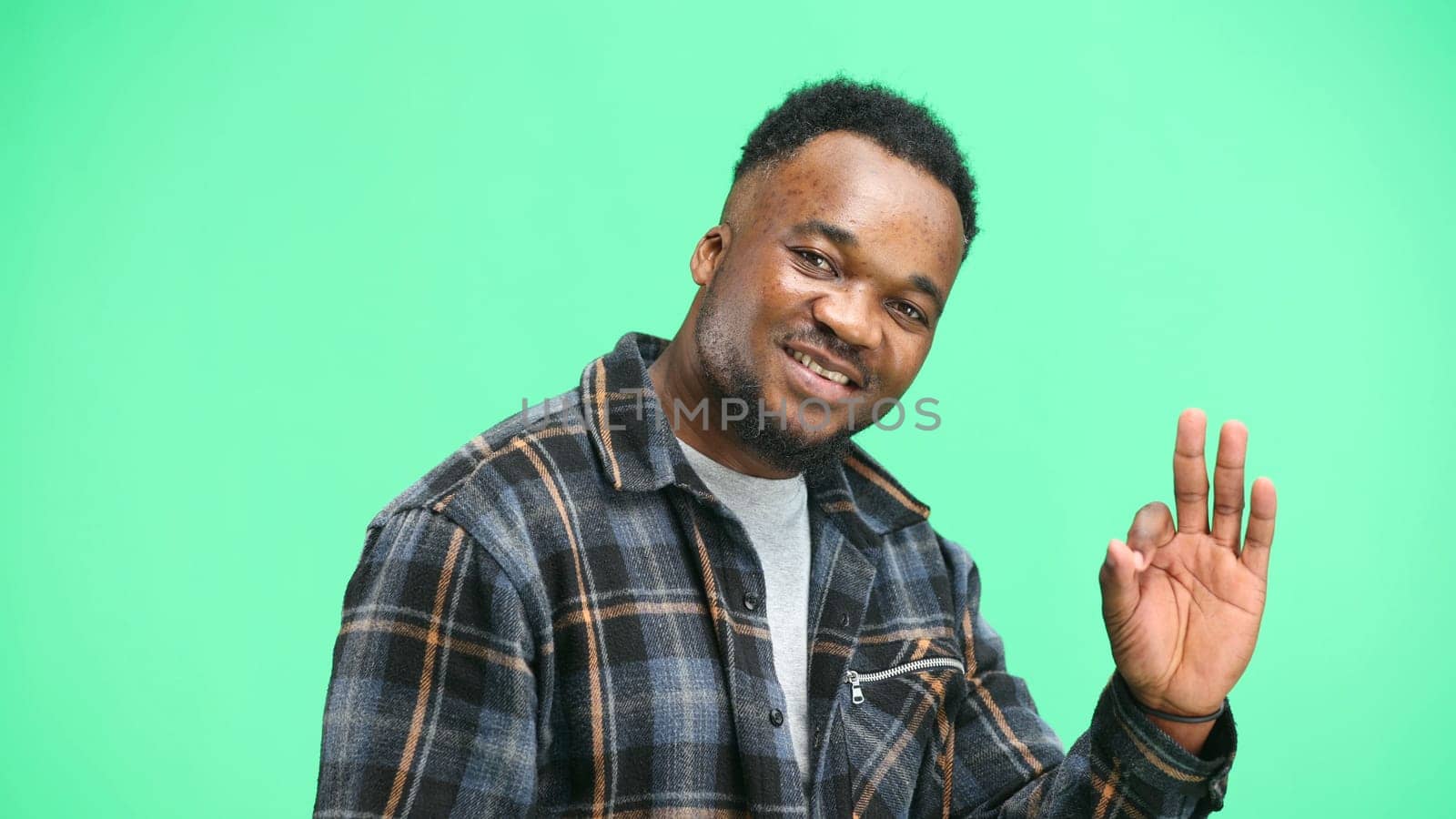 A man, close-up, on a green background, shows an ok sign.