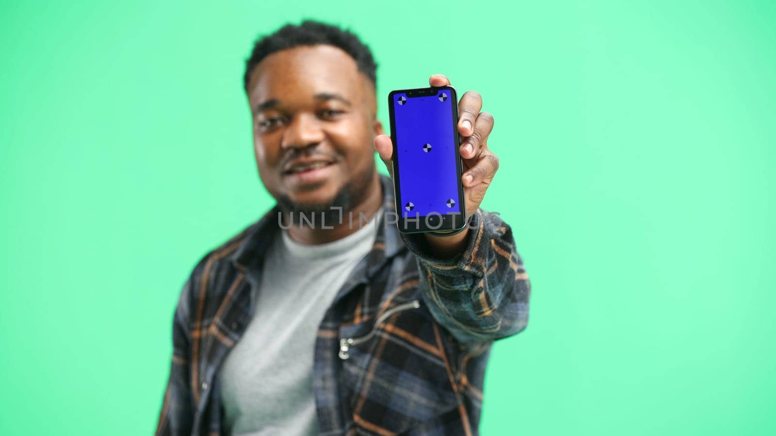 A man, close-up, on a green background, shows a phone by Prosto