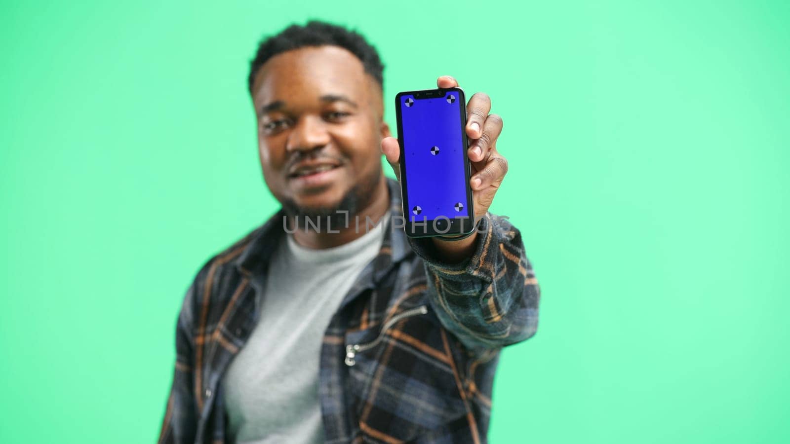 A man, close-up, on a green background, shows a phone.