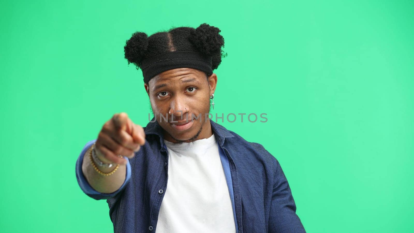 A man, close-up, on a green background, points forward.