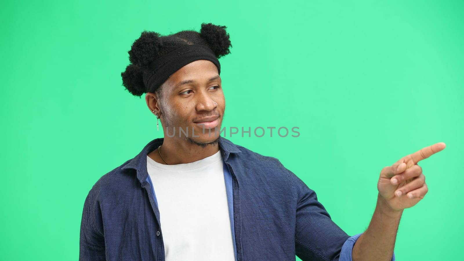 A man, close-up, on a green background, points to the side.