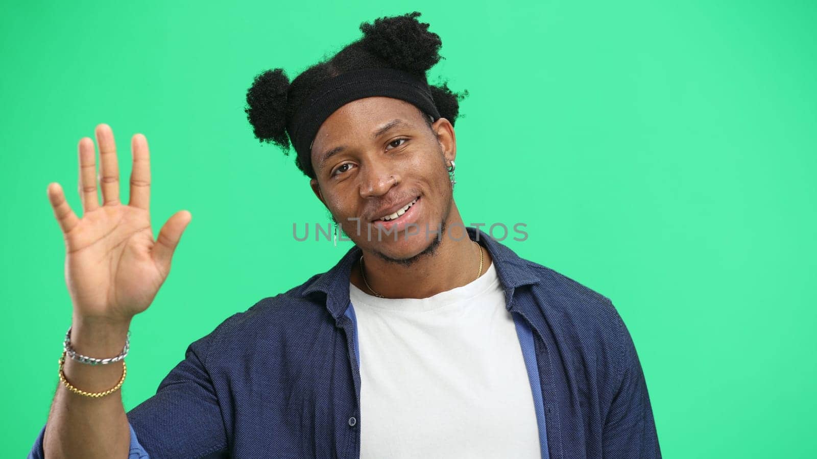 A man, close-up, on a green background, waving his hand.