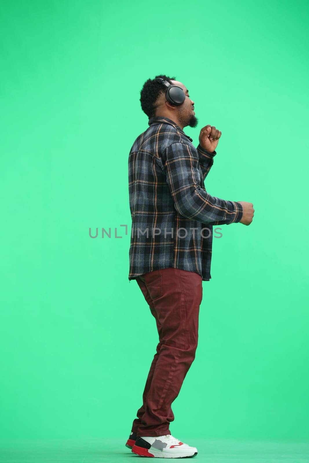 A man, full-length, on a green background, wearing headphones by Prosto