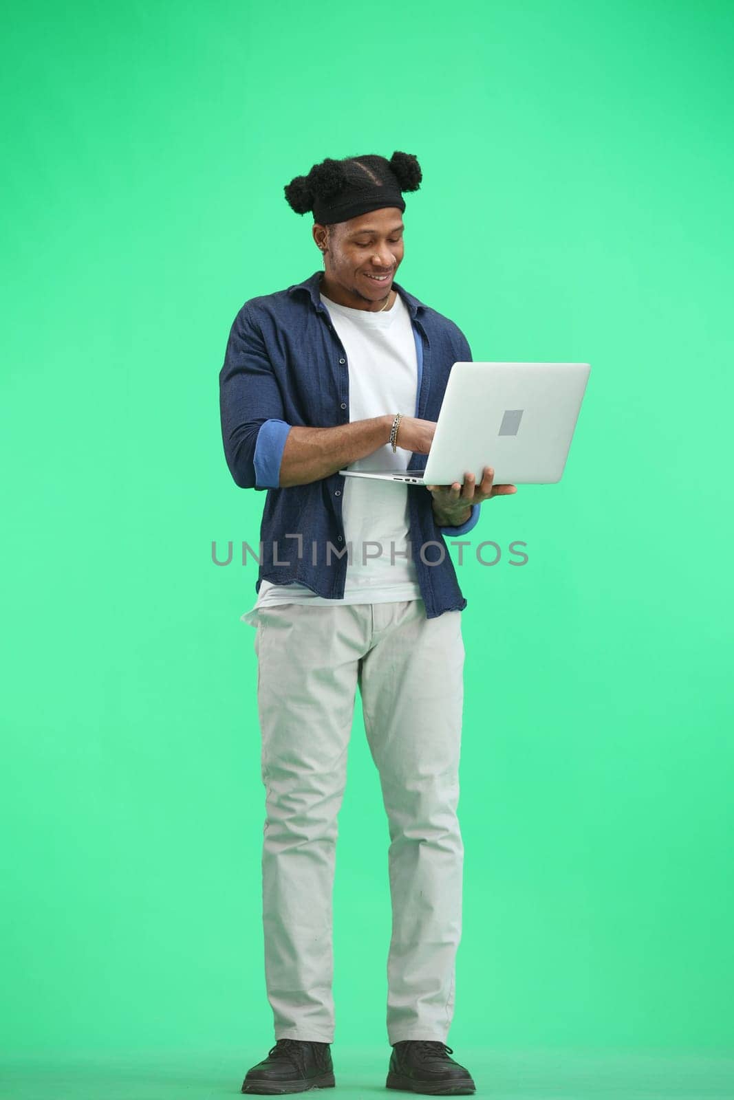 A man, full-length, on a green background, uses a laptop by Prosto