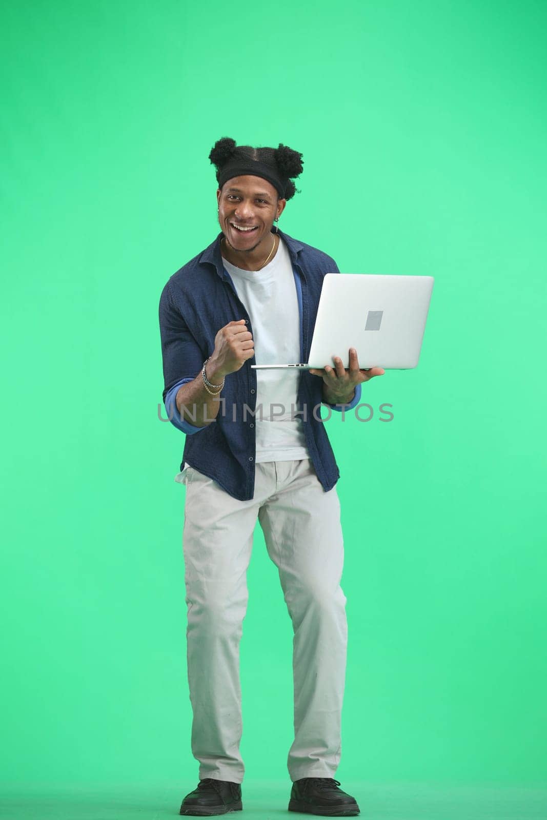 A man, full-length, on a green background, uses a laptop by Prosto