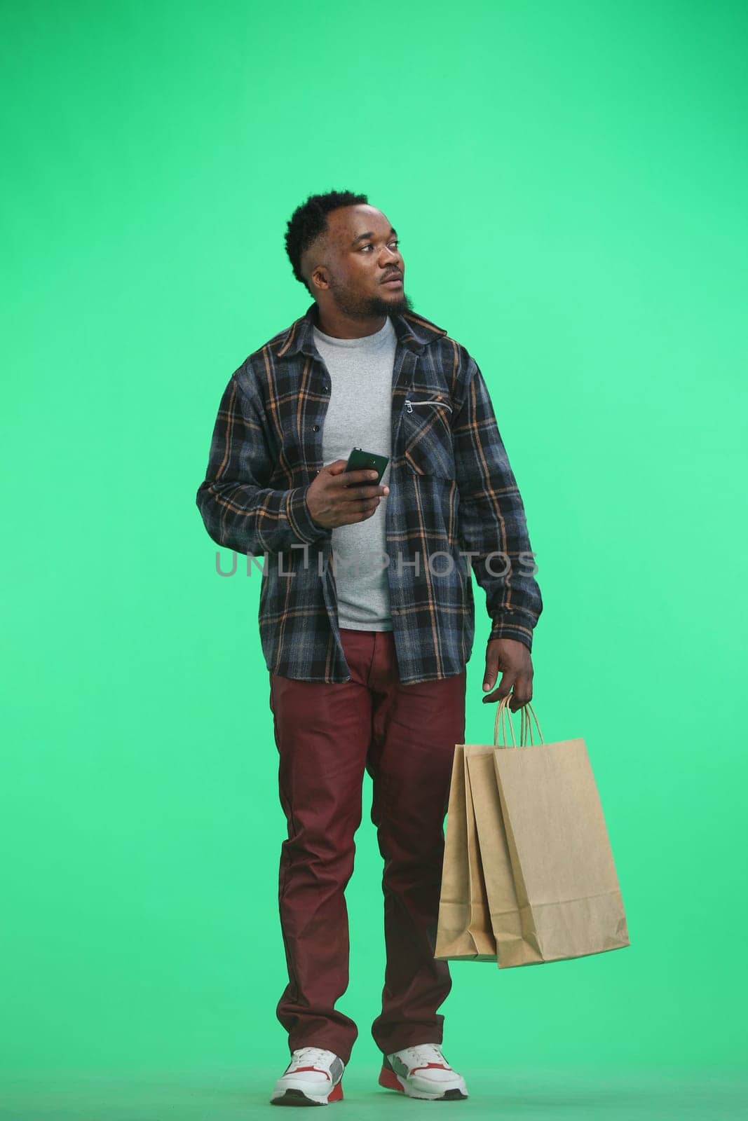 A man, full-length, on a green background, with bags, shows a phone by Prosto