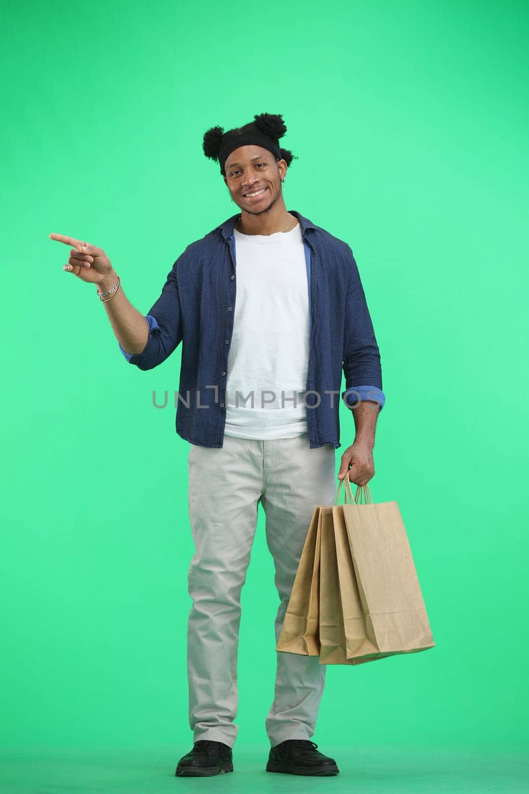 A man, full-length, on a green background, with bags, points to the side by Prosto