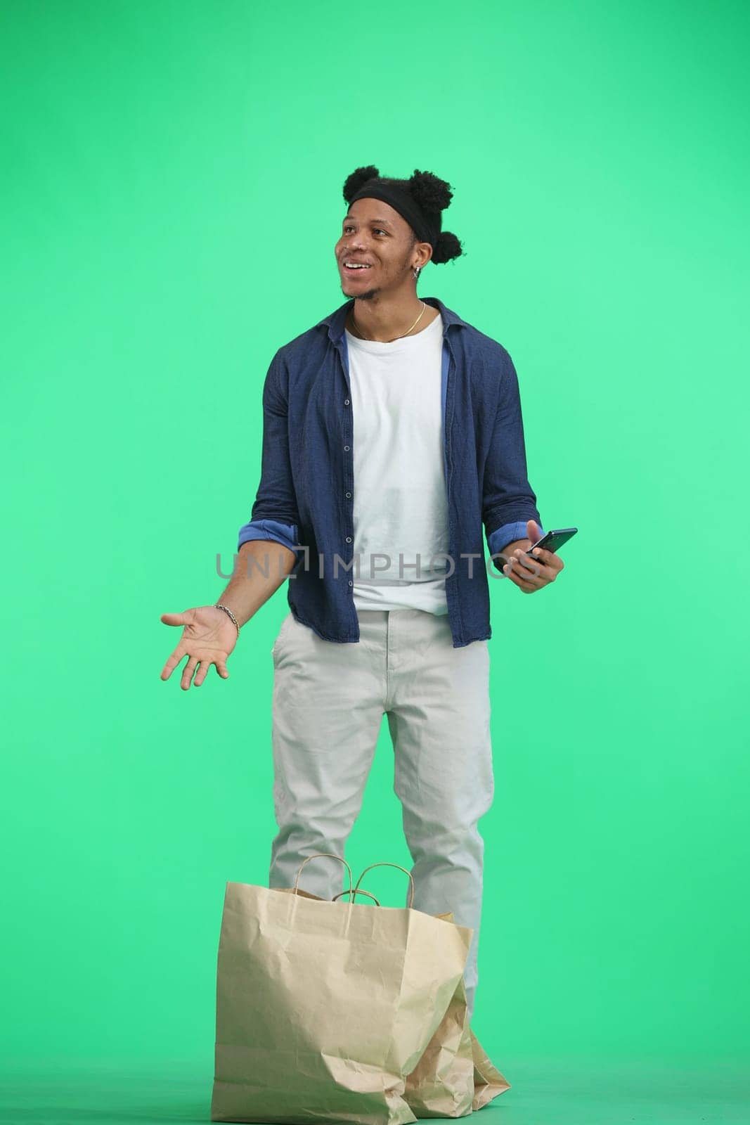 A man, full-length, on a green background, with bags and a phone by Prosto