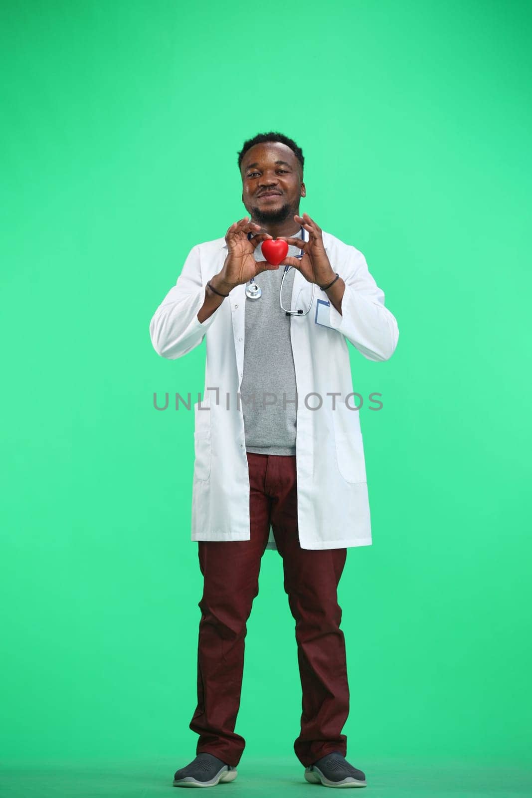The doctor, in full height, on a green background, shows the heart.