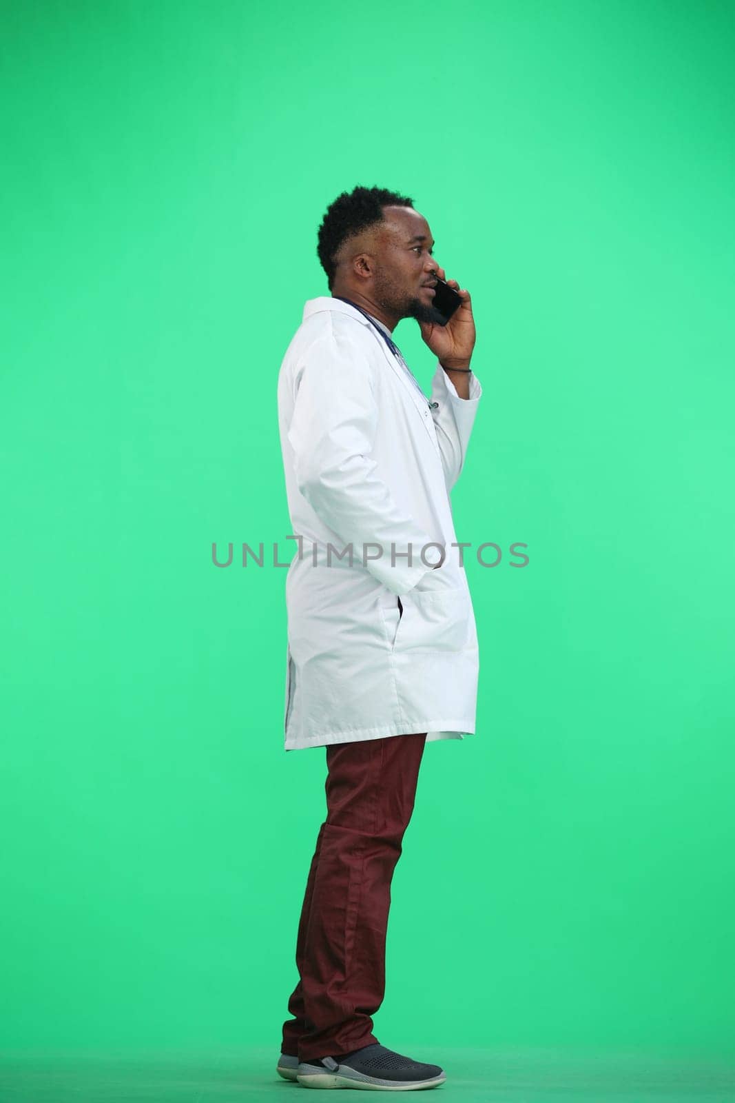 The doctor, in full height, on a green background, talking on the phone.