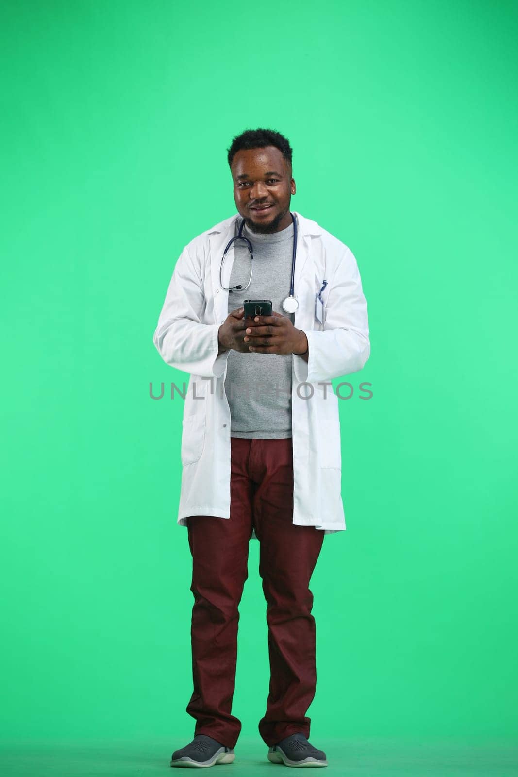 The doctor, in full height, on a green background, uses a phone by Prosto
