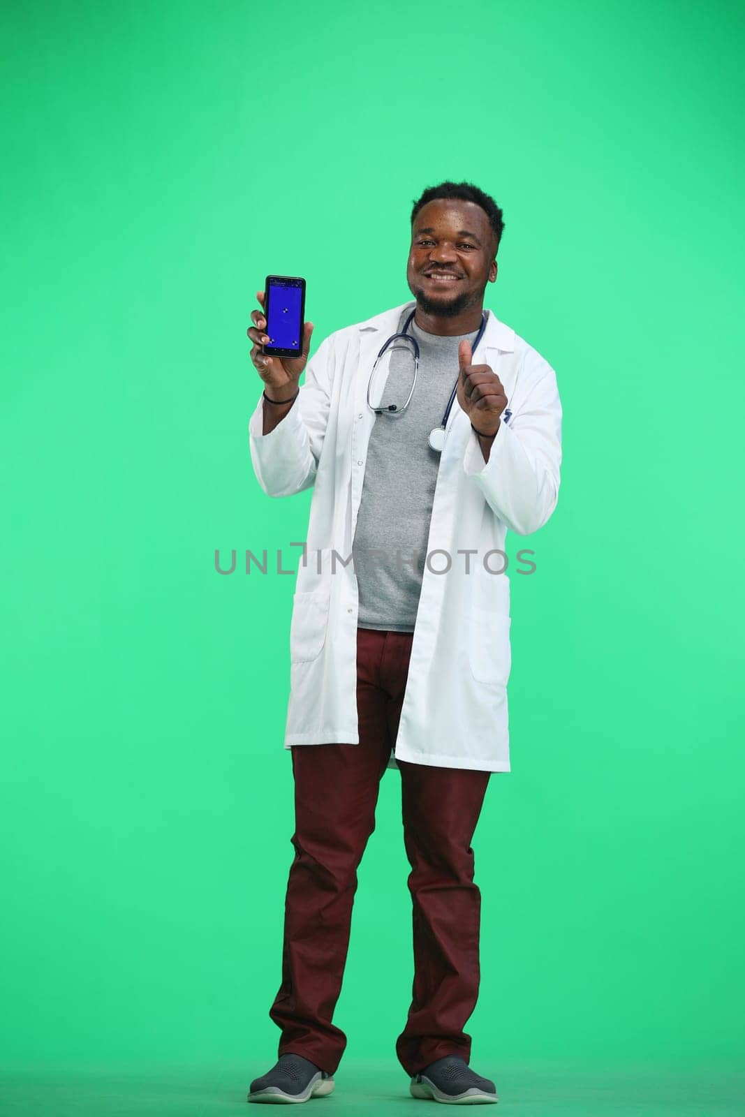 The doctor, in full height, on a green background, shows the phone.