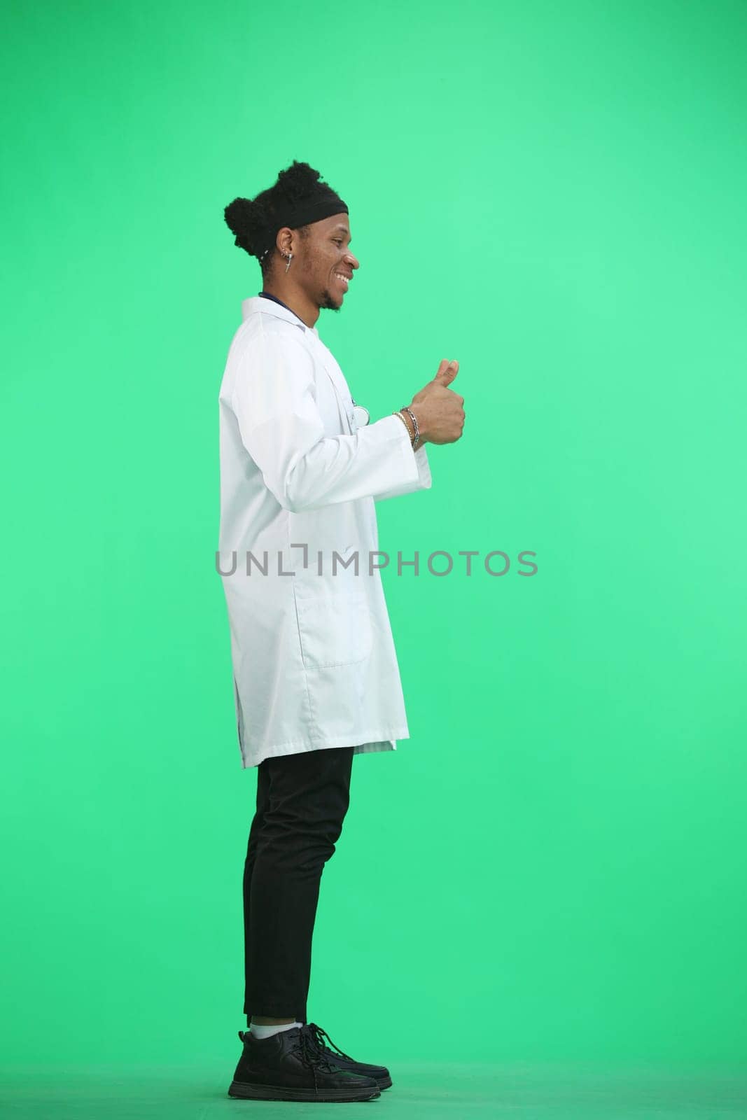 The doctor, in full height, on a green background, shows his fingers up.