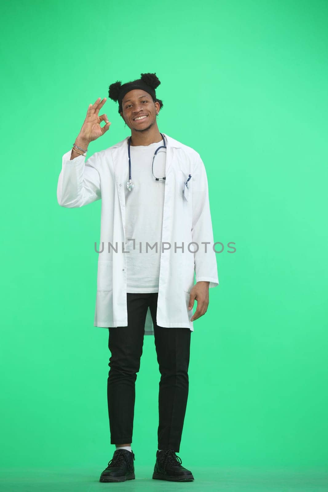 The doctor, in full height, on a green background, shows the ok sign.