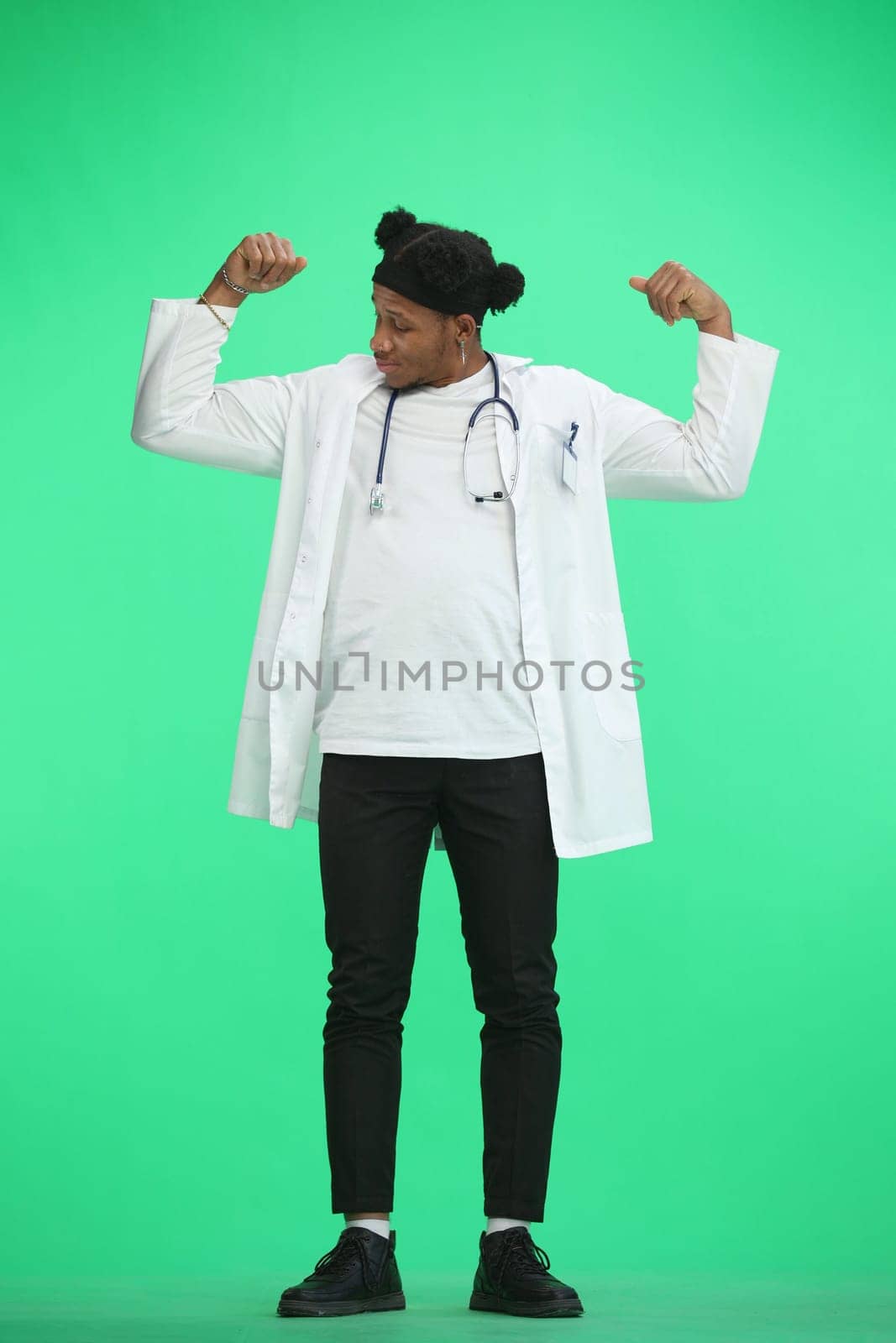 The doctor, in full height, on a green background, shows strength.