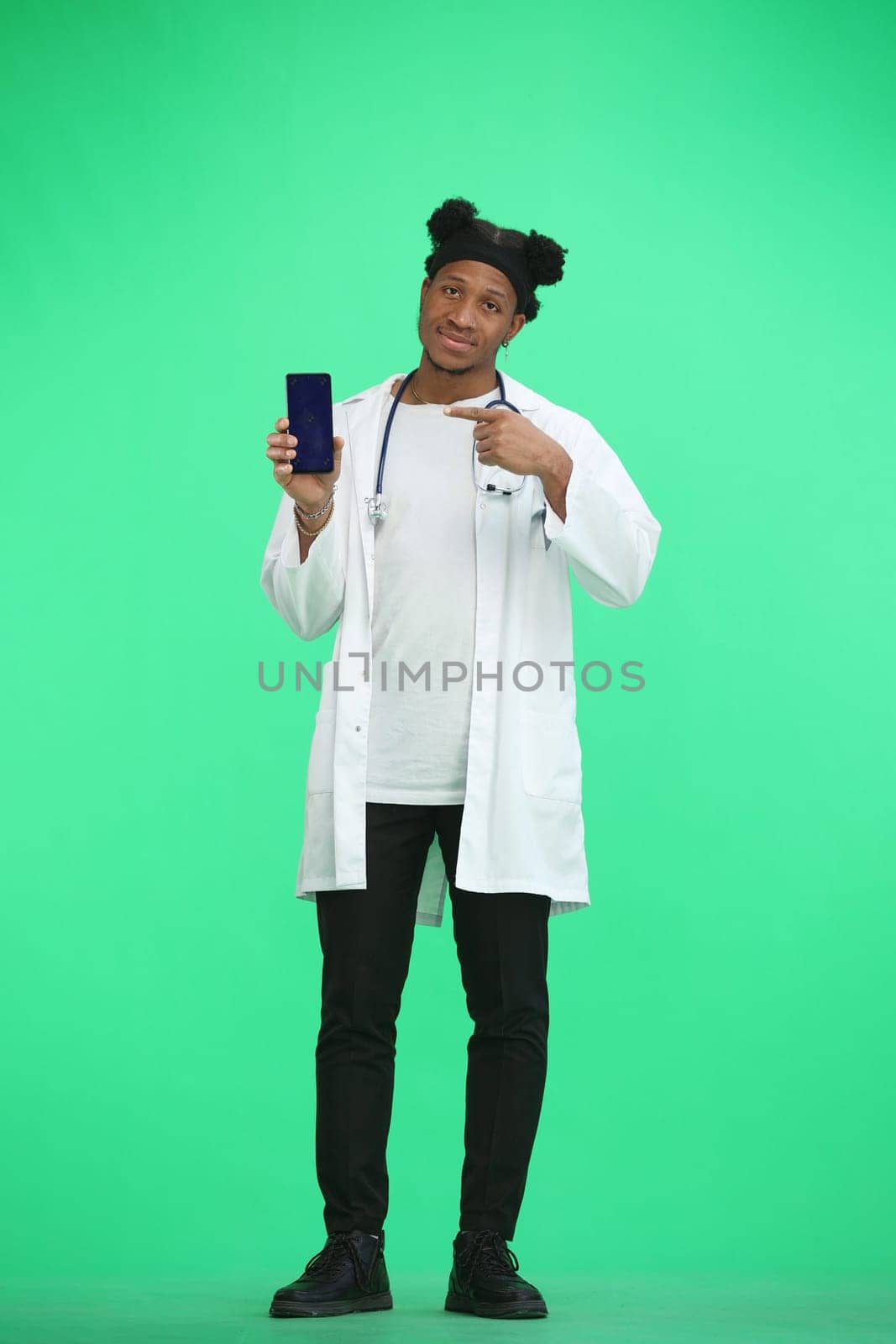 The doctor, in full height, on a green background, shows the phone by Prosto