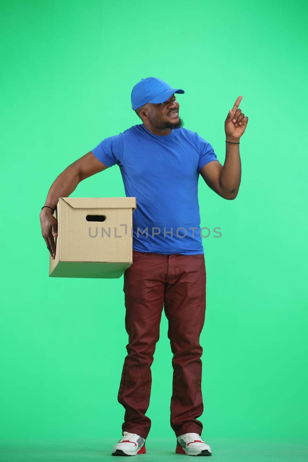 The deliveryman, in full height, on a green background, with a box, points to the side.