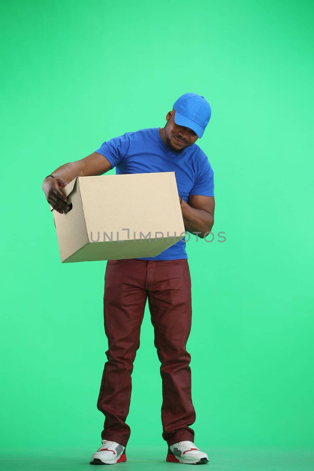 The deliveryman, in full height, on a green background, looks at the box.